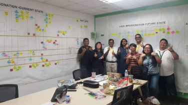 Team posing in front of current-state and future-state value stream maps on the wall